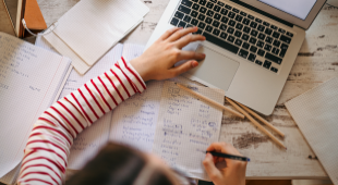 Woman in a striped shirt working on an online course with a laptop, notebook, and pencils.