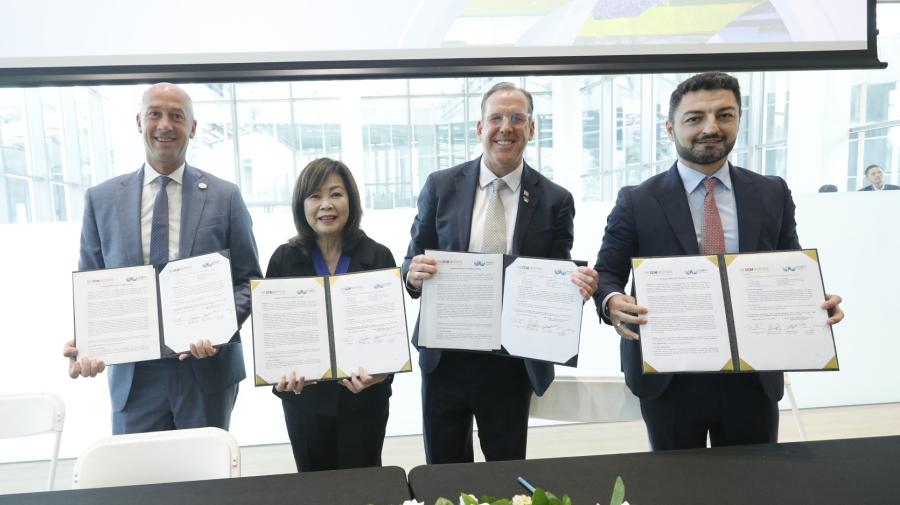 Four professionals in suits hold certificates and smile in a modern office with a city view.