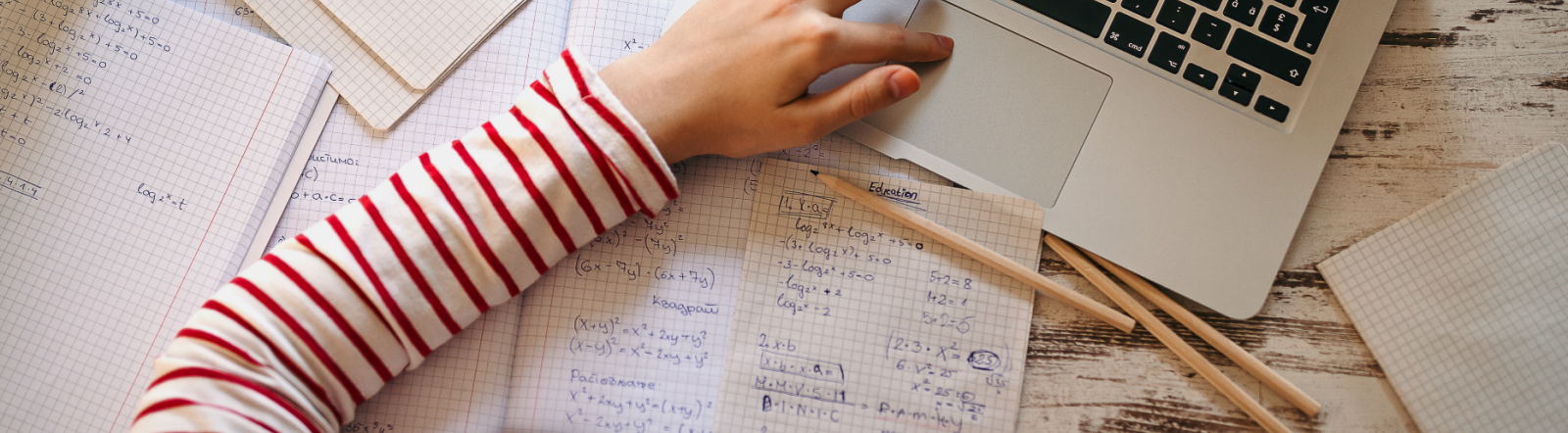 Woman in a striped shirt working on an online course with a laptop, notebook, and pencils.