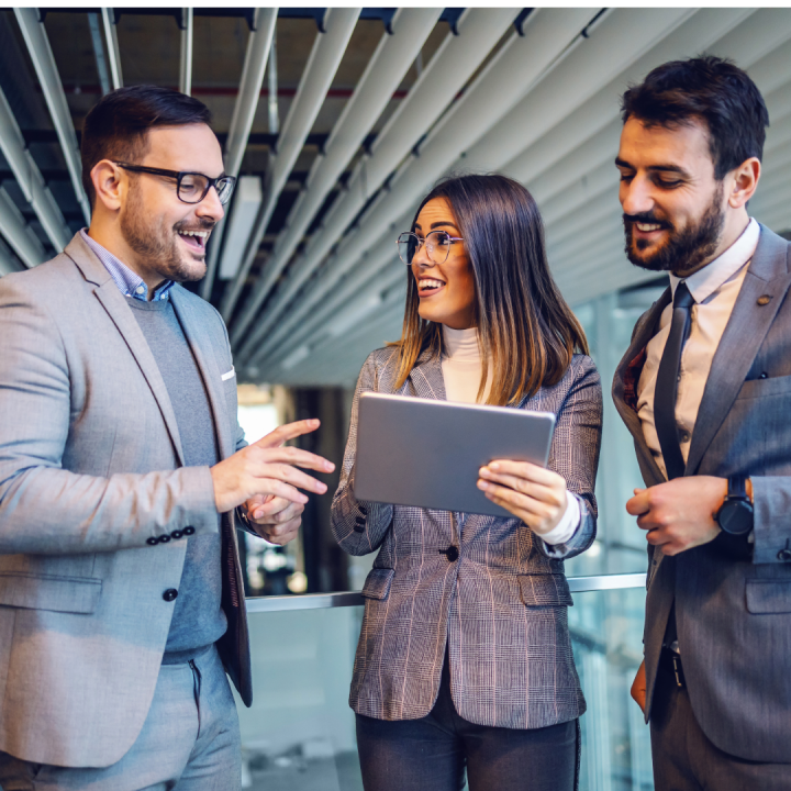 Three young professionals looking at a tablet computer and smiling.