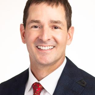 Brunette man wearing a black suit and red patterned tie.