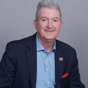 Middle aged man wearing a dark blue blazer and light blue shirt.